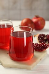 Tasty pomegranate juice in glasses and fresh fruits on white wooden table, closeup
