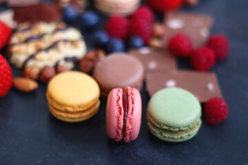 Macarons, chocolate, cookies, berries and various nuts on dark blue background. Selective focus.