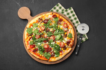 Delicious vegetarian pizza and cutter on black table, top view