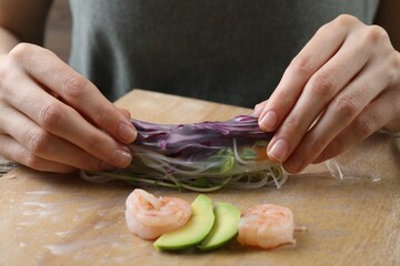 Woman wrapping spring roll at table with products, closeup