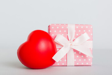 gift box with red bow and red heart on colored background. Perspective view. Flat lay