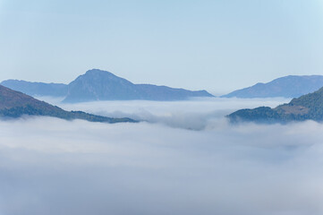 A tranquil dawn where mist weaves through mountain peaks, creating a dreamlike landscape.