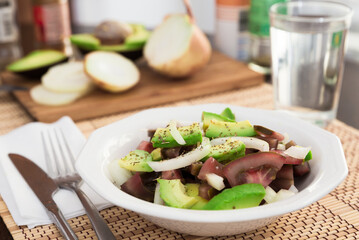 salad of black tomatoes, avocado and onions in white ceramic bowl