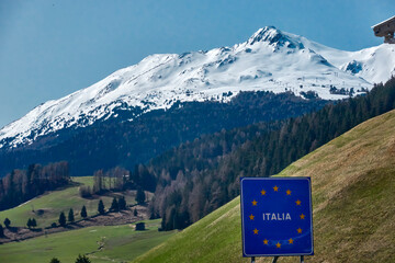 Snow-covered mountain peaks behind green alpine meadows on the border between Austria and Italy