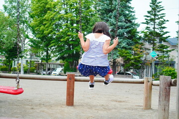 夏休みの公園でブランコ遊びを楽しんでいる女の子の後ろ姿