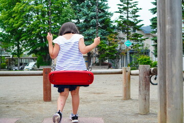夏休みの公園でブランコ遊びを楽しんでいてブランコから降りた女の子の後ろ姿、 - obrazy, fototapety, plakaty