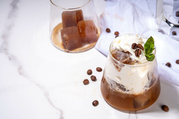 Latte coffee summer cocktail. Cold brewed iced cappuccino coffee,  with whipped foamy cream or non-dairy milk and frozen coffee ice cubes, on white kitchen background copy space