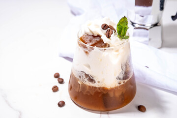 Latte coffee summer cocktail. Cold brewed iced cappuccino coffee,  with whipped foamy cream or non-dairy milk and frozen coffee ice cubes, on white kitchen background copy space