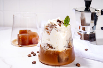 Latte coffee summer cocktail. Cold brewed iced cappuccino coffee,  with whipped foamy cream or non-dairy milk and frozen coffee ice cubes, on white kitchen background copy space