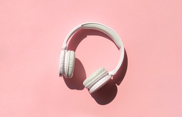 Wireless white headphones  on the pink background close up. Listening to music concept
