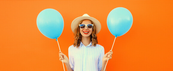 Portrait of happy smiling young woman with blue balloon wearing summer straw hat on orange