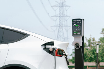 Electric vehicle or EV car recharge battery at charging station connected to power grid tower...