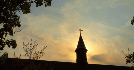 Birds at dusk, circling Catholic church spire, manifest as faith messengers against serene sunset...