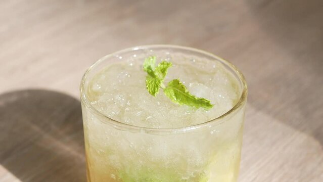 roating view of a glass of refreshment ice mojito cocktail alcohol drink with lime and mint leaves on wooden table