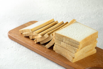 A close up of a stack of white bread slices on a wooden cutting board.