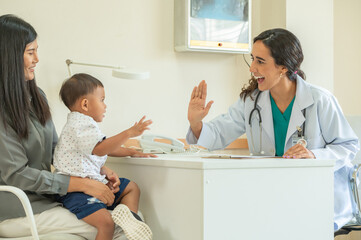 Pediatrician giving a high five to a young patient while the mother looks on smiling