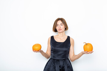 Young attractive woman in black beautiful dress holding pumpkins isolated on white background. Halloween celebrating concept