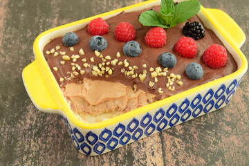Homemade oatmeal tiramisu with melted dark chocolate topped with fresh berries, chopped almond and mint leaf on serving dish