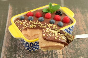 Homemade oatmeal tiramisu with melted dark chocolate topped with fresh berries, chopped almond and mint leaf on serving dish