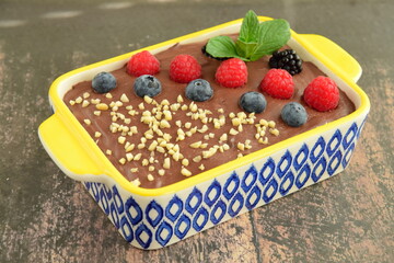 Homemade oatmeal tiramisu with melted dark chocolate topped with fresh berries, chopped almond and mint leaf on serving dish