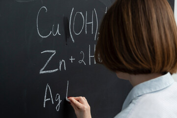 Female student writing the formula of a chemical reaction on the blackboard	