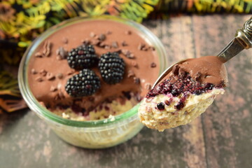 Overnight oatmeal with mashed blackberry and chocolate cream, on top garnish with fresh blackberry and cacao nibs