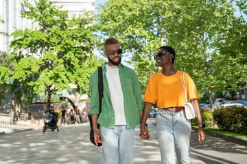 Happy pleased african american couple strolls through city, chatting smiling enjoy time together on...