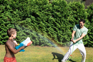Father and son spending time in backyard playing water guns on hot sunny weather	