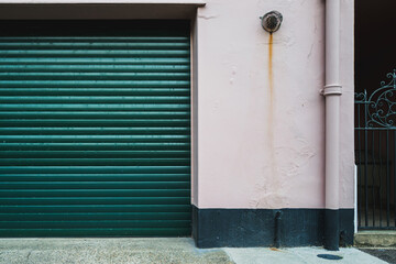 Abstract view of closed roller door leading to a private garage located on a narrow English street. A side gate can be seen leading to the back of the property.