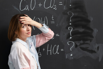 Confused female student writing the formula of a chemical reaction on the blackboard