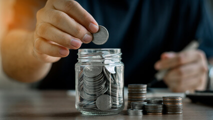 Money saving concept. hand holding coins putting in jug glass. money spending concept, profitable...