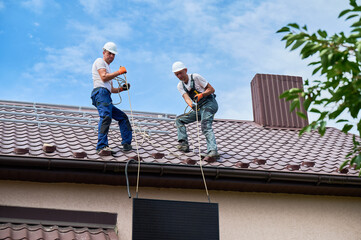Men workers installing solar panel system on roof of house. Electricians in helmets lifting up...
