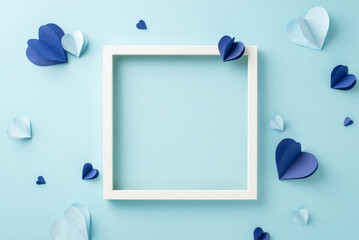 A creative flat lay with paper hearts and an empty frame arranged on a soft blue backdrop, ideal...
