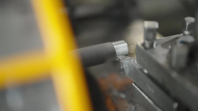 Close-up of a metal rod being threaded in a lathe machine, metalworking and industrial manufacturing. Cutting metal parts at factory workshop. Making thread