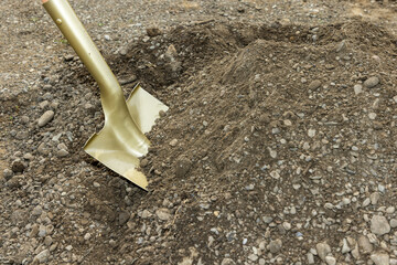 Golden spade shovel in heavy gravel dirt for ground breaking 