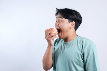 Young Asian Man Excited To Eat Apple Wearing Casual Clothing Isolated On White Background