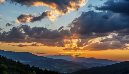 Obraz premium A stunning sunset over the mountain range with the sun shining through the clouds, creating a beautiful afterglow in the sky