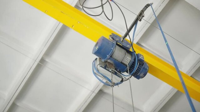 Overhead view of electric hoist on a yellow beam in an industrial workshop. Crane cathead for lifting and moving materials in factory, warehouse. 