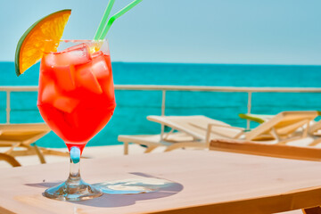 A glass of red cocktail on the table against the background of the sea on the beach or on the deck of a yacht or cruise ship