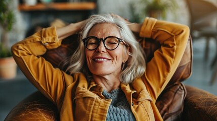 Obraz premium Smiling attractive senior woman relax at home, enjoy lazy weekend seated on armchair with hands behind head, breathe fresh air, daydream, relish peaceful leisure, feel stress free.