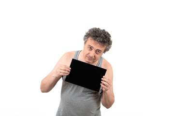 A shaggy gray-haired middle-aged man with stubble in a sleeveless T-shirt holds a black sign...
