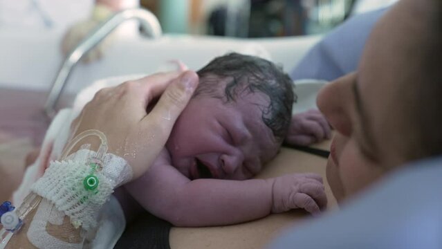 Mother welcoming her newborn baby after giving birth, infant crying on mother's chest after childbirth, initial cries, first seconds of life at hospital