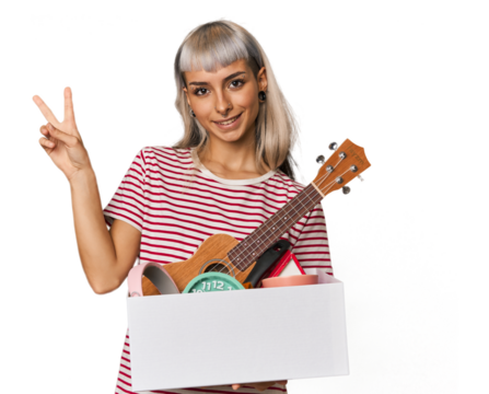 Caucasian young woman holding moving box joyful and carefree showing a peace symbol with fingers.