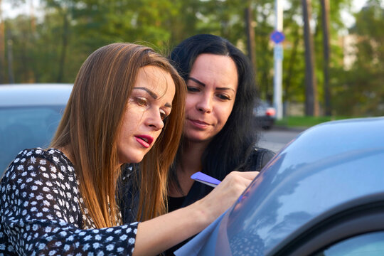 Young woman with her friend signing a document on the trunk of a car
