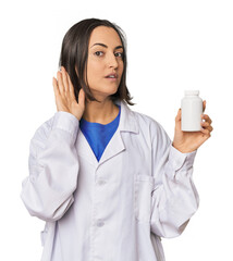Young Caucasian female pharmacist with pills trying to listening a gossip.