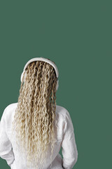 Trendy female wearing white shirt in headphones on head, listening to music, dancing, enjoy free time. Stylish woman with blonde long hair, back view, no face trend, colored background