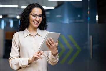 A joyful professional woman in smart attire, using a digital tablet in a modern office setting, reflecting productivity and connectivity.
