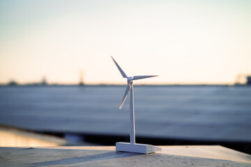 A wind turbine is standing on a ledge overlooking a body of water. The scene is serene and...