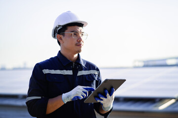 A worker wearing a hard hat and safety glasses is holding a tablet in his hands. He is focused on...