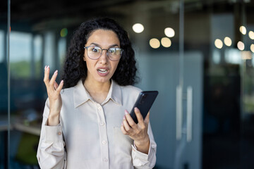 A businesswoman appears upset and frustrated while holding a smartphone in a contemporary office...